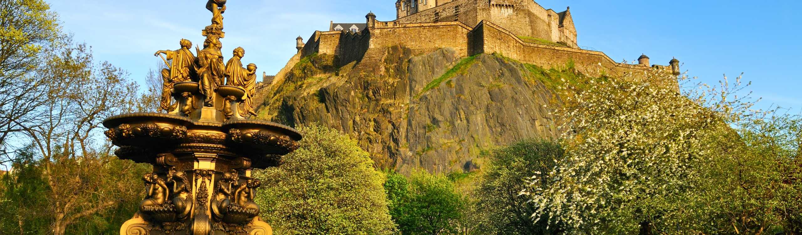 Panoramic sunset view over the historic Edinburgh skyline showing Castle Rock and Old Town monuments under a golden sky.